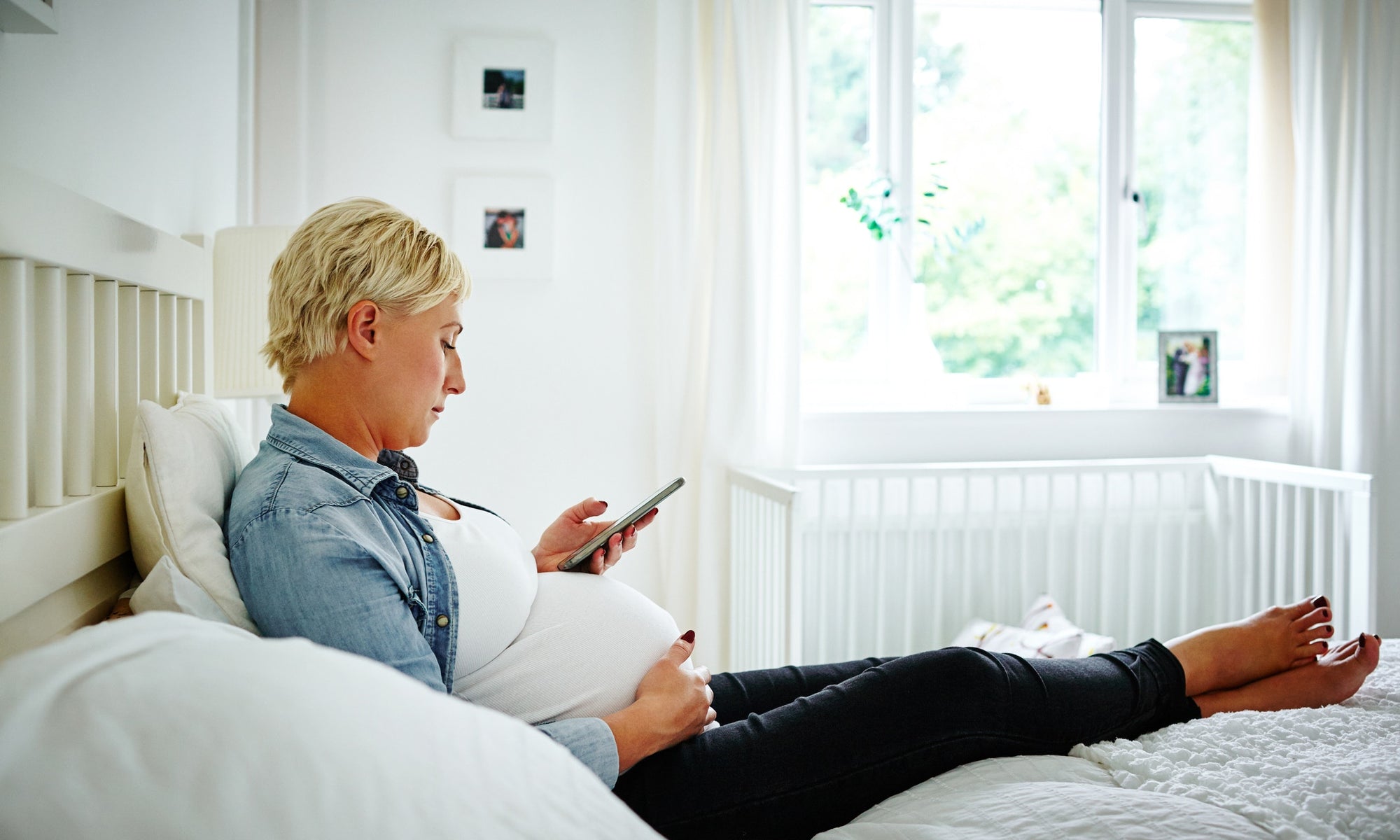 pregnant women sitting on bed and using phone