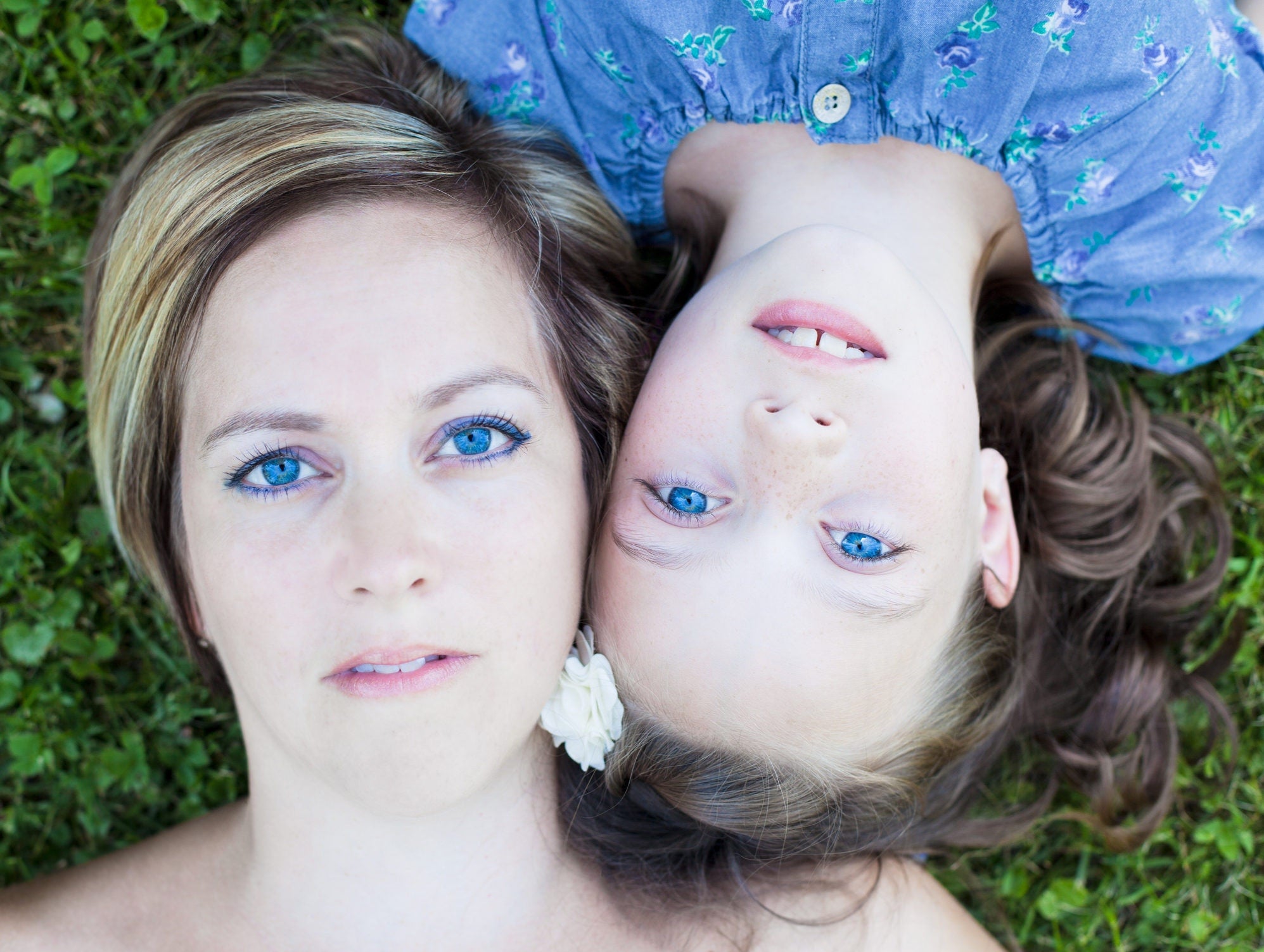 mother and daughter with blue eyes lying on field head to head with legs in opposite directions