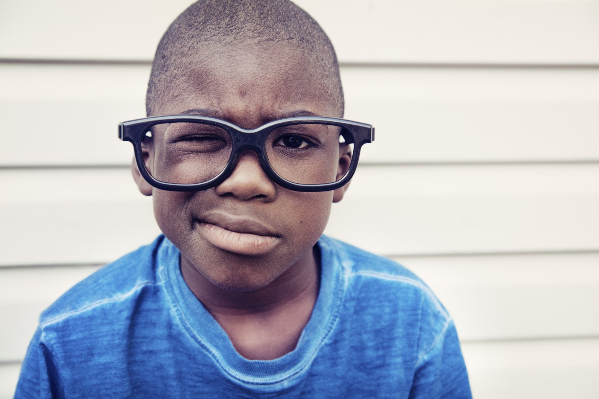 little boy with one eye closed wearing black framed glass