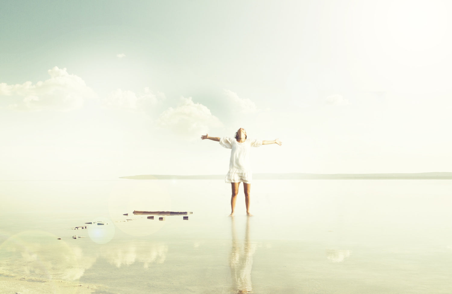 Young woman standing on the shore of scenic lake with her hands raised. 