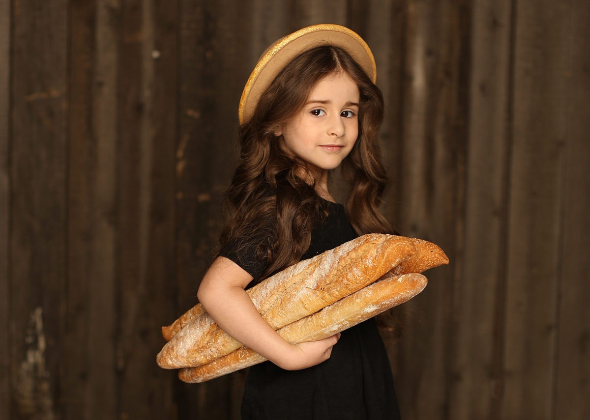 little girl with long brown hair wearing hat and holding loaf of bread