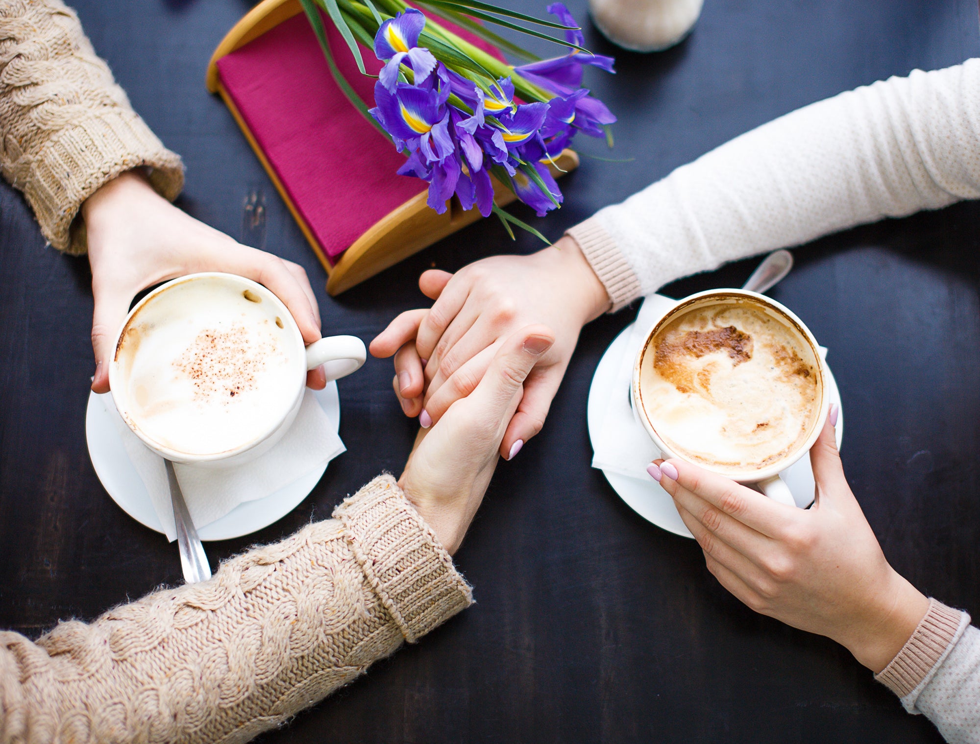 two person holding hands between two cups of coffee above table,