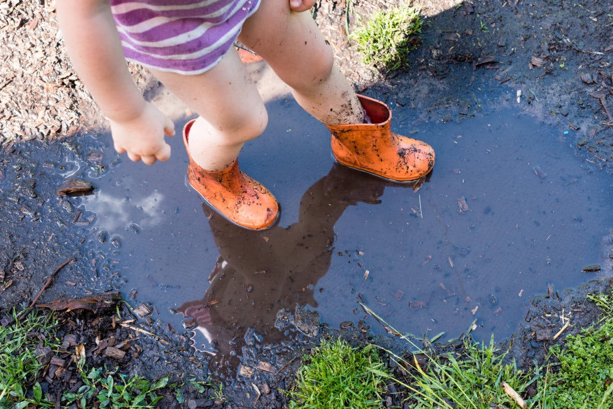 Little child wearing rain boots playing in the muddy puddle