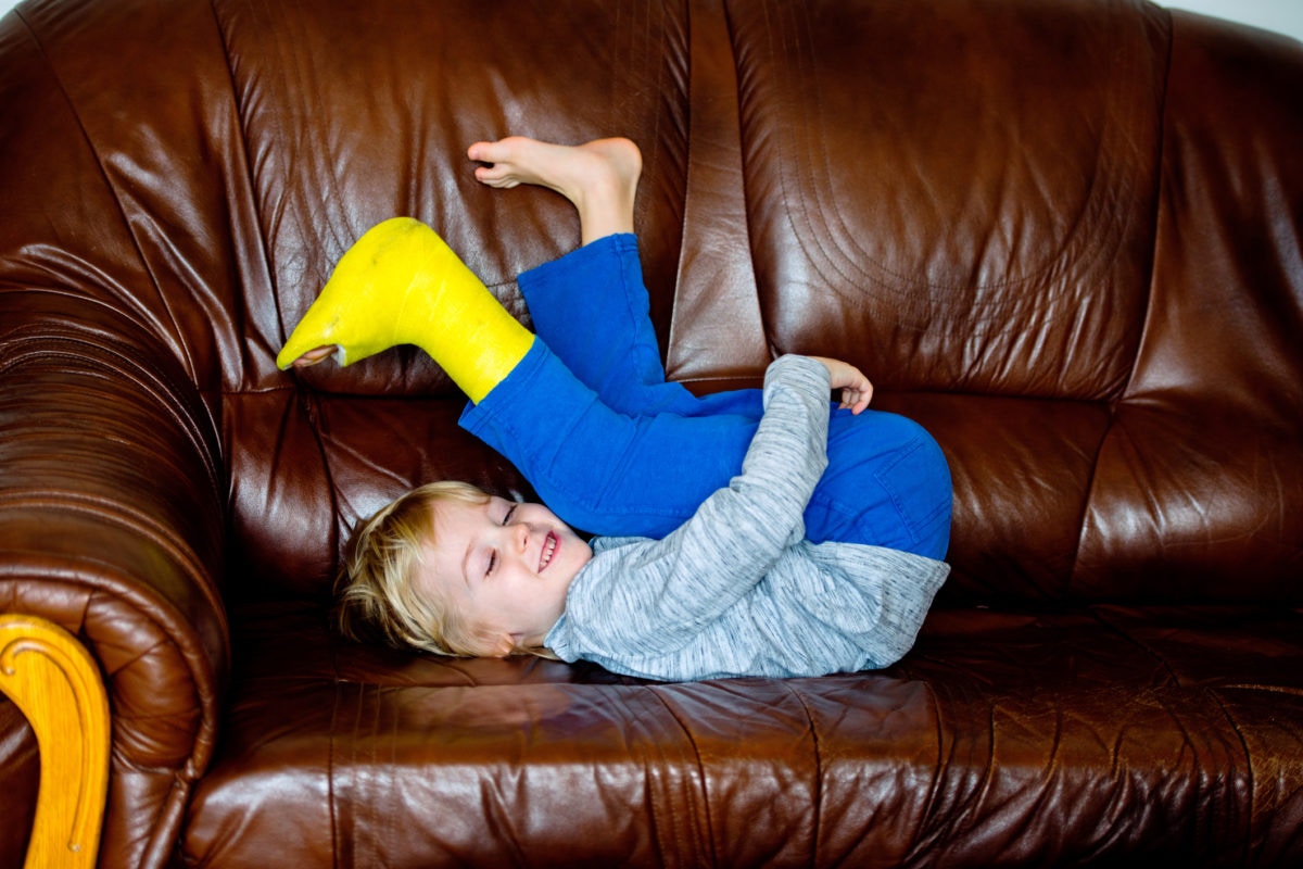 A kid is enjoying in a sofa with wearing plaster of paris in one leg