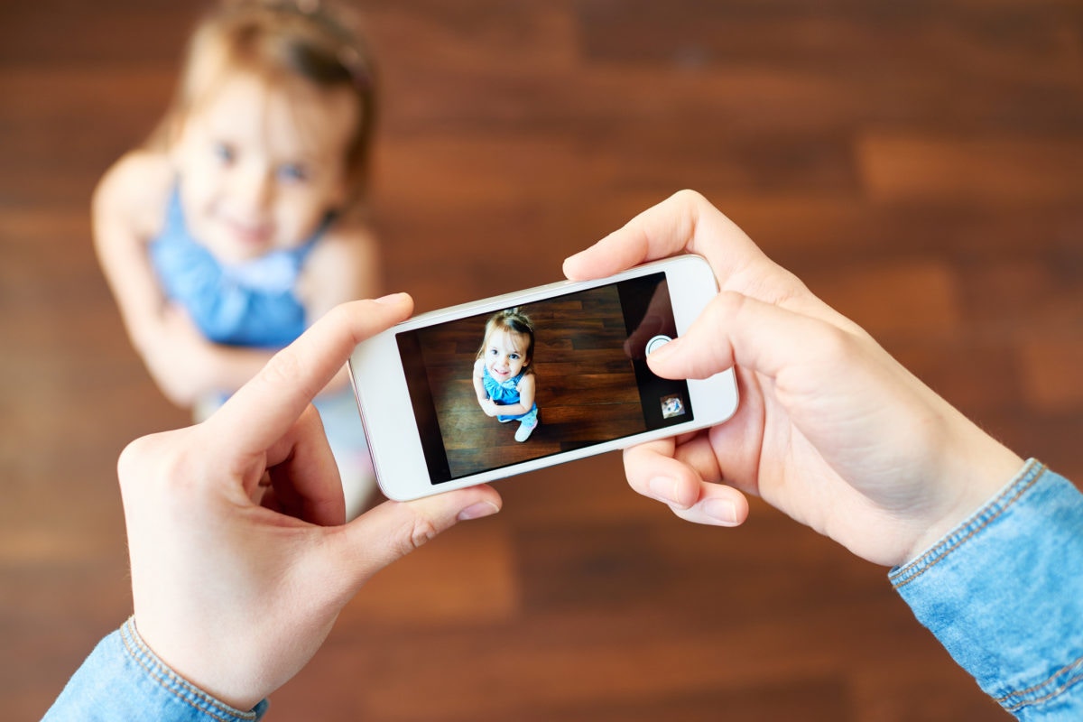 Parent holding phone taking photo of  daughter on smartphone