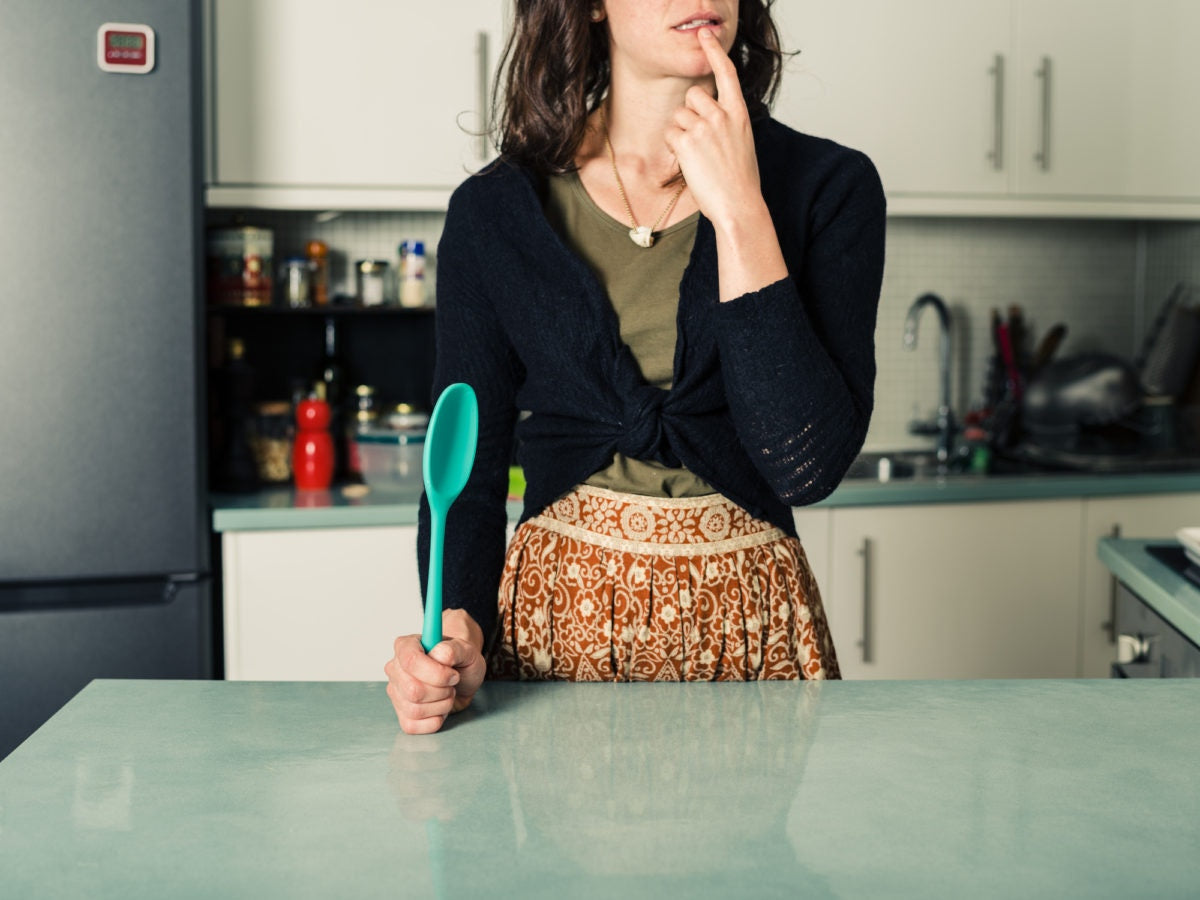 Confused woman with spoon in kitchen.