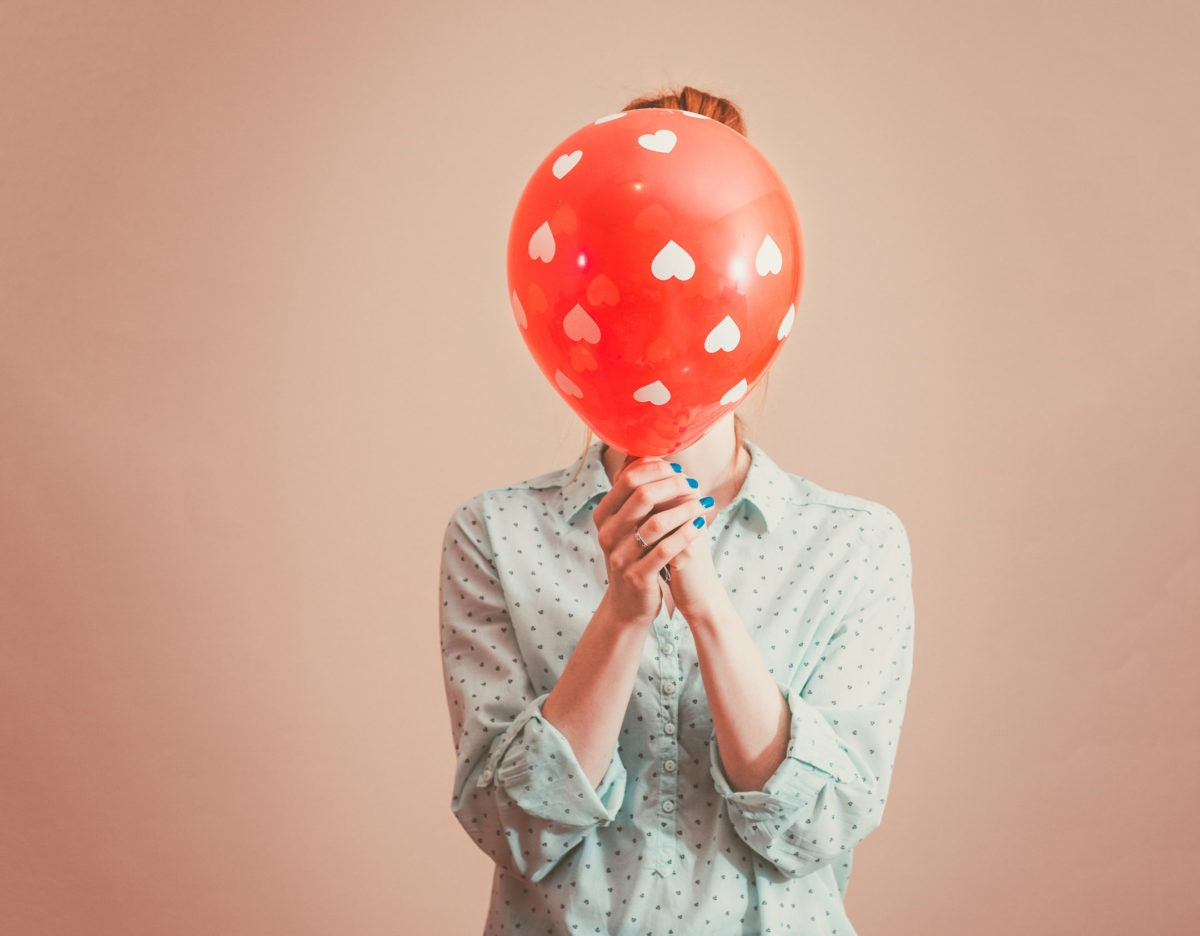 young girl covering face with balloon