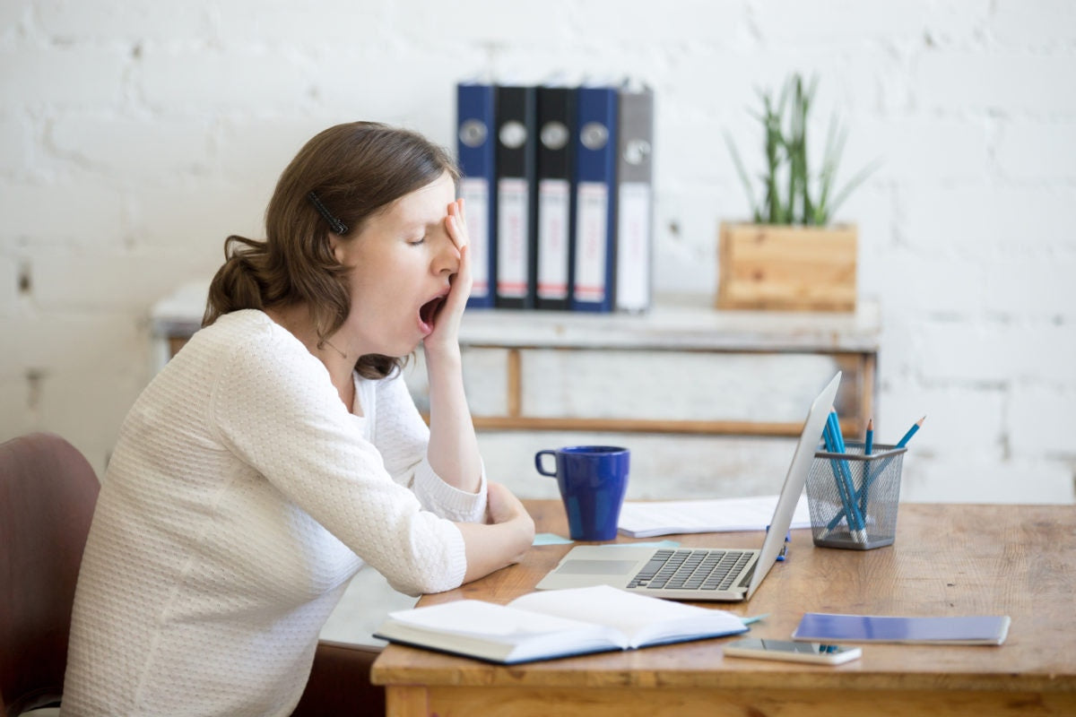 Tired woman yawning, sitting at table with laptop, lazy to work
