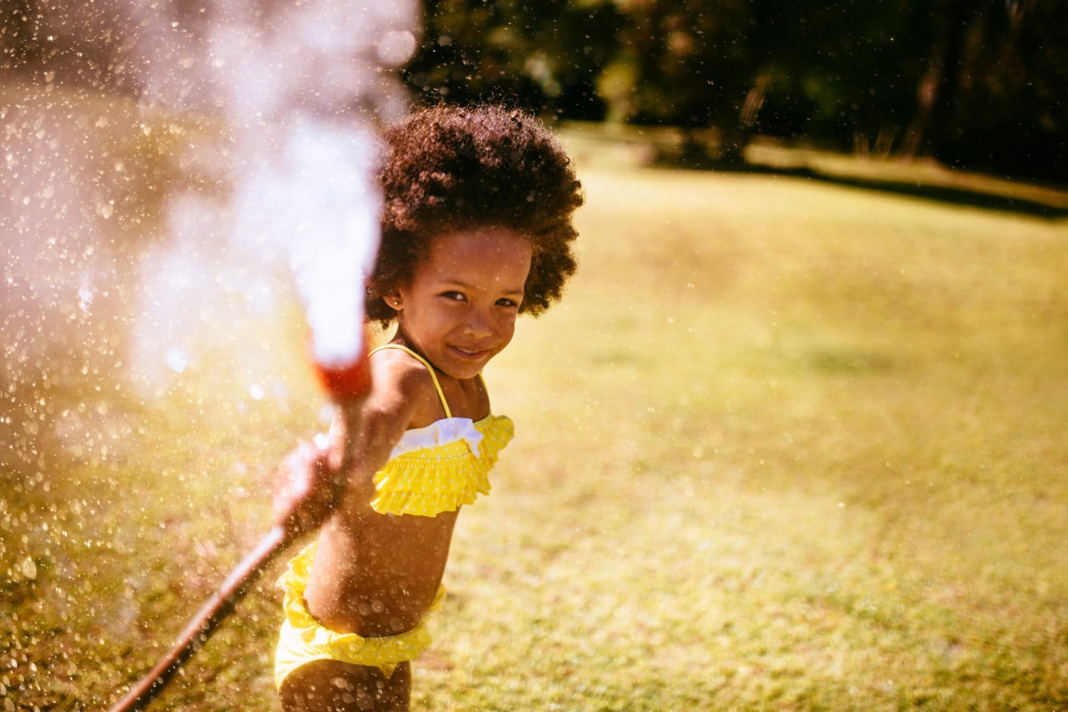 Little girl playing with water hose at the garden