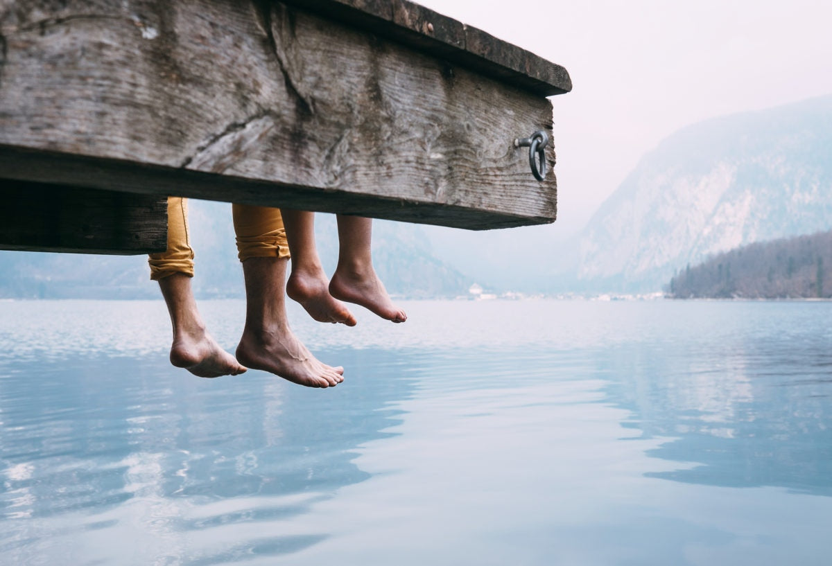 father and son sitting, dangling feet over tranquil lake dock