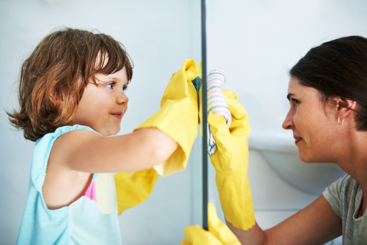 A mother and a kid is cleaning glass with a mirror image reflection