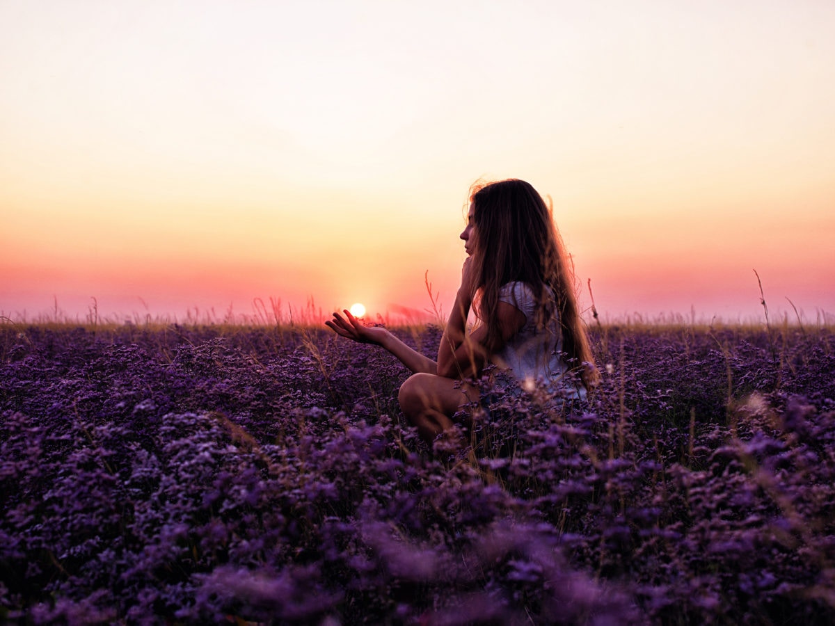 A girl is sitting on open land in a sunset time by holding sun on one hand
