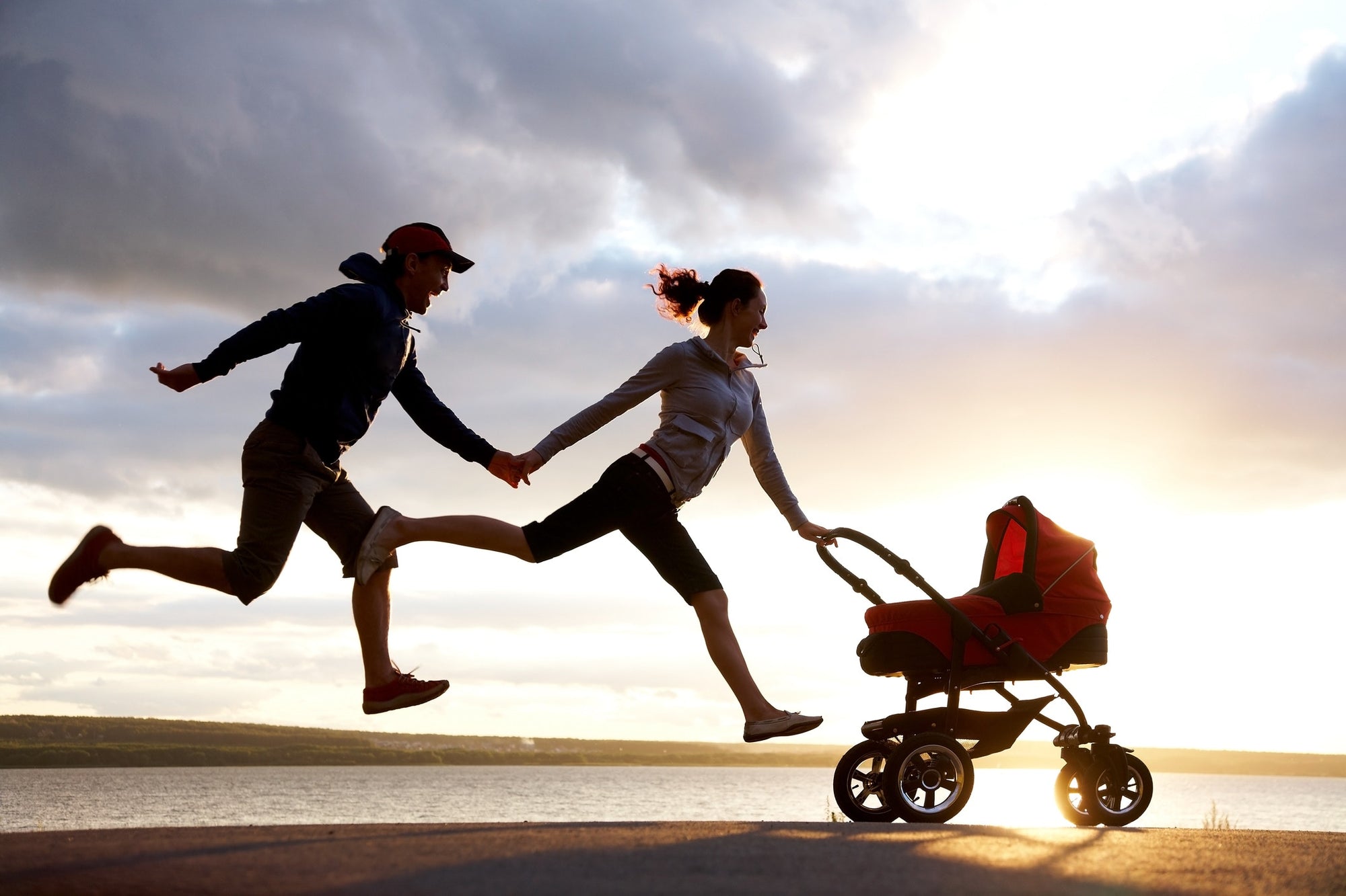 parents jumping in air with child in stroller