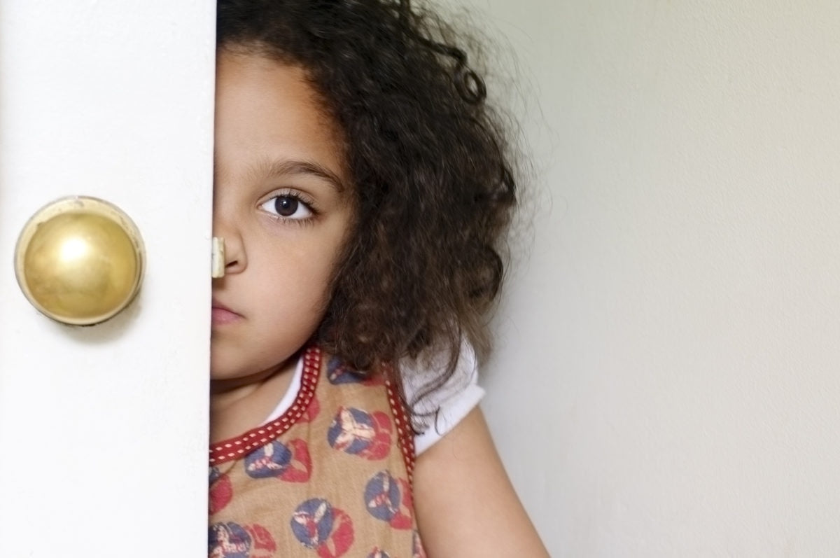 Scared little Girl Hiding Behind Door At Home