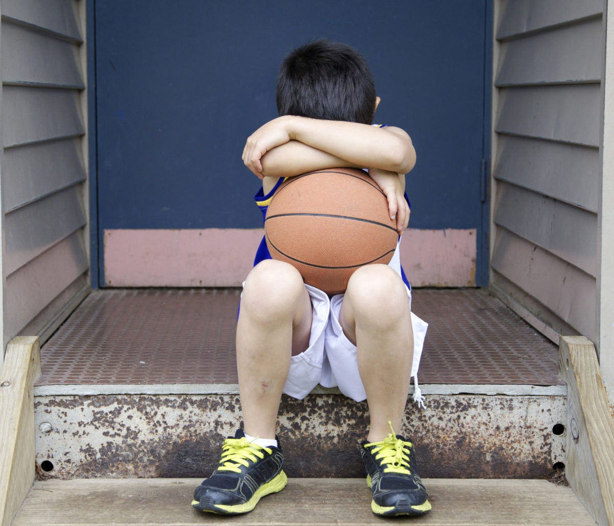 Upset boy covered his face with basketball sitting on the stairs