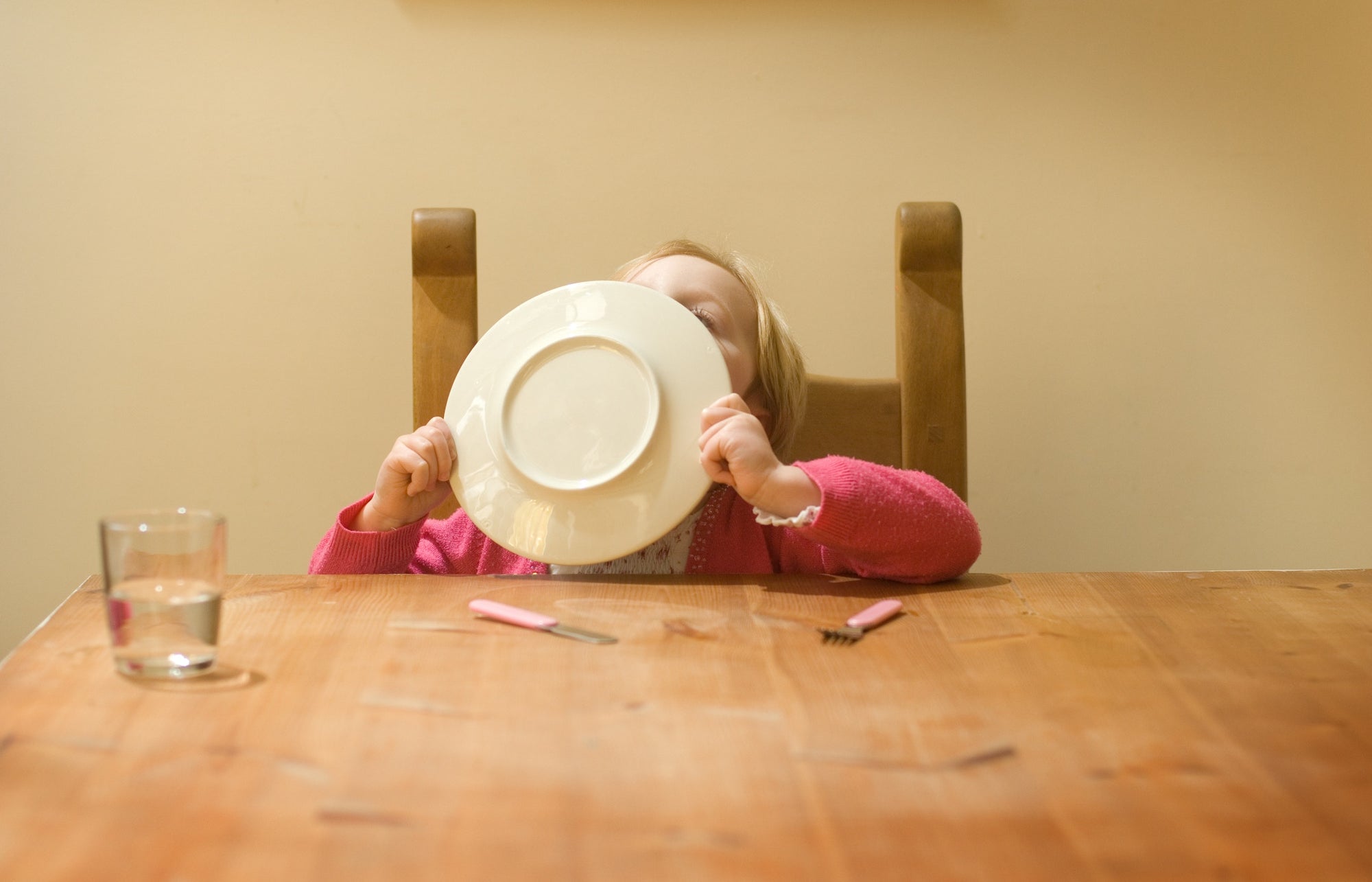 Child finishing food, cleaning plate using tongue, hiding face