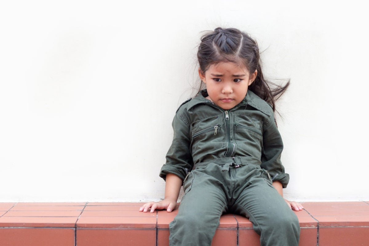 sad little girl sitting on the floor over white wall
