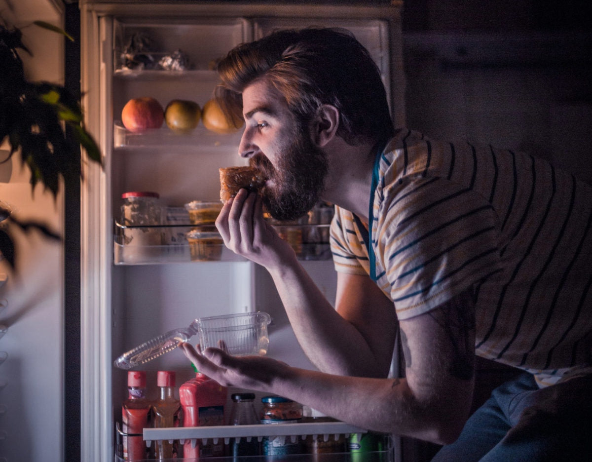 man eating piece of cake near open fridge