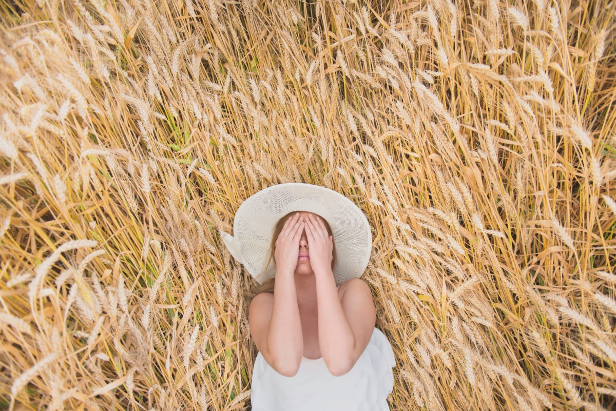 woman laying on a grass field covering her face with hands