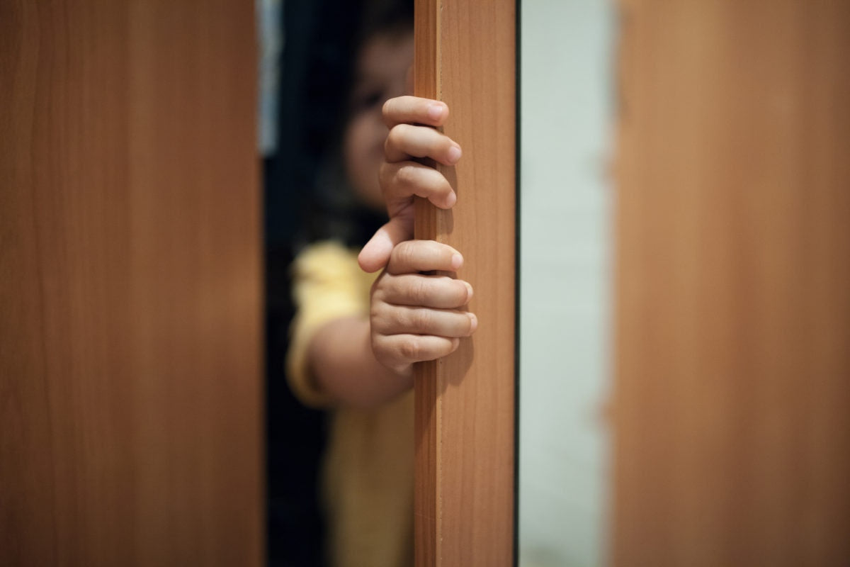 Child is standing behind door and opening slightly