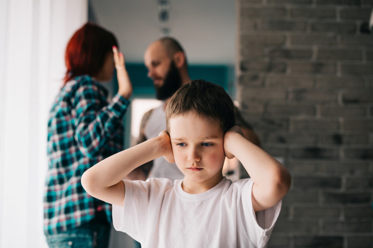 Sad little boy covering ears while his parents arguing at home