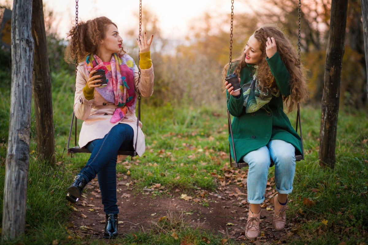Two girls sitting on swing chair and talking