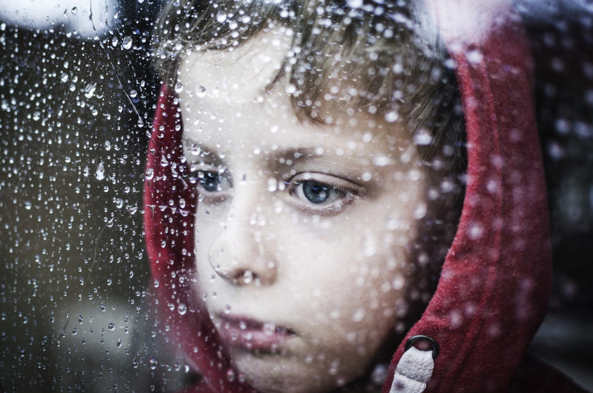 A child looking from inside a window at the rainfall