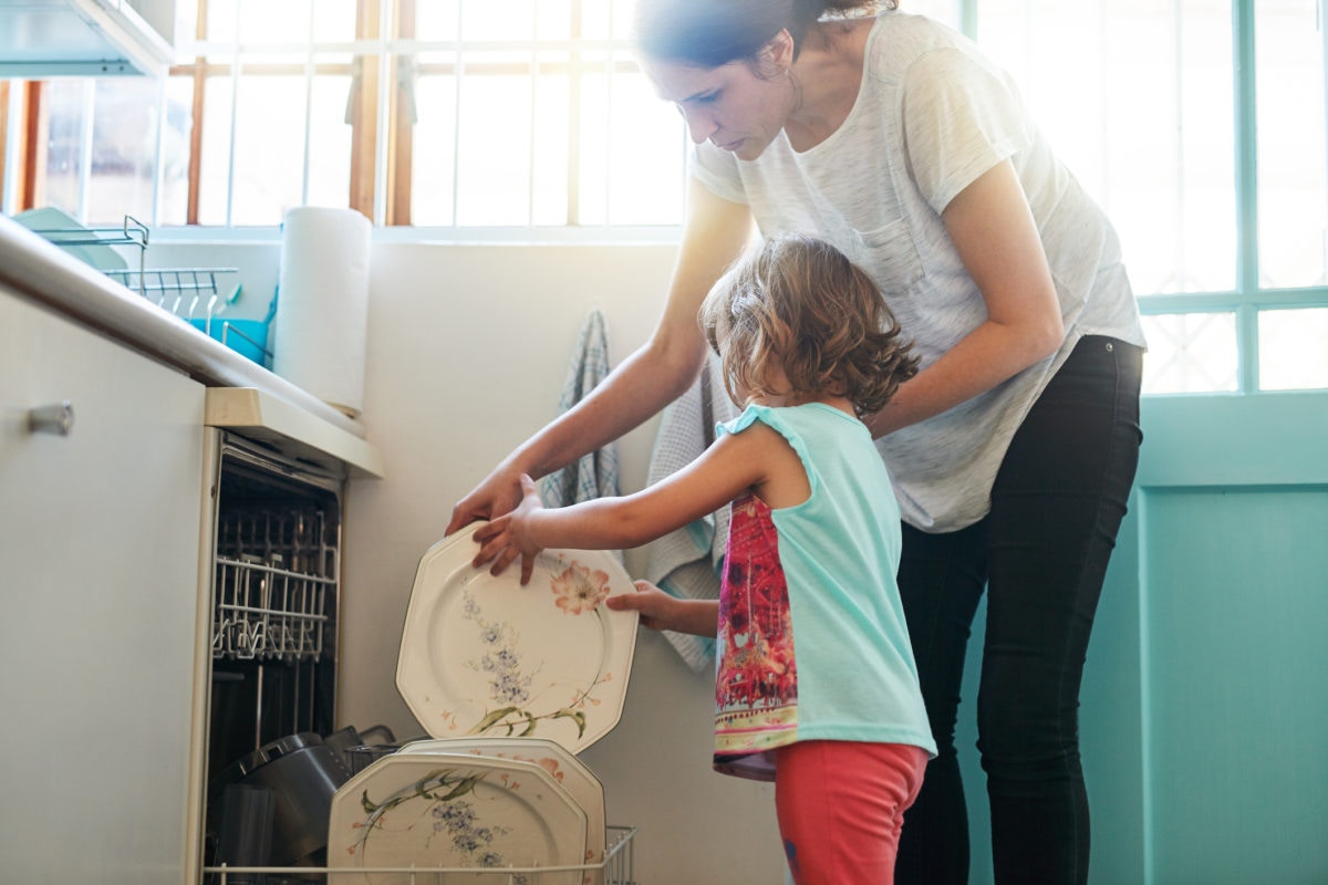 A mother guiding her child to place plate on dishwasher