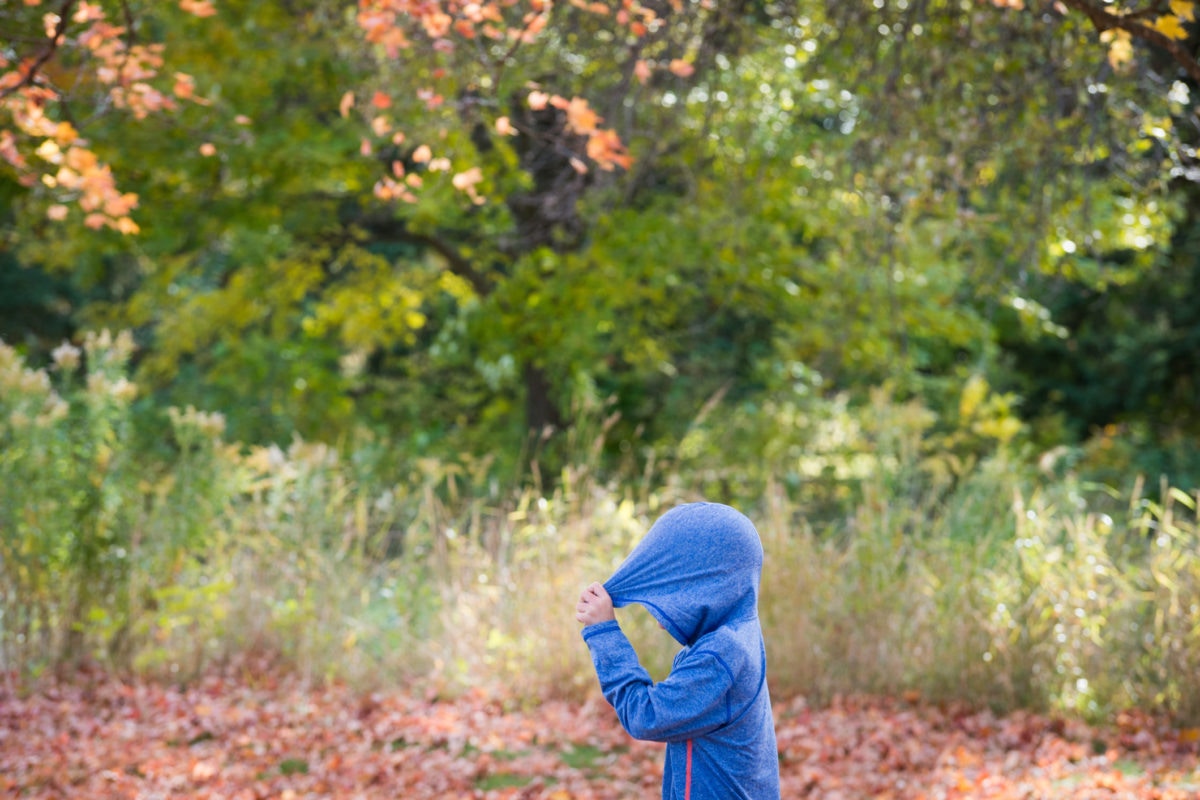 kid covering his head with hoodie in field
