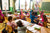Kindergarten teacher and children with hands raised in classroom