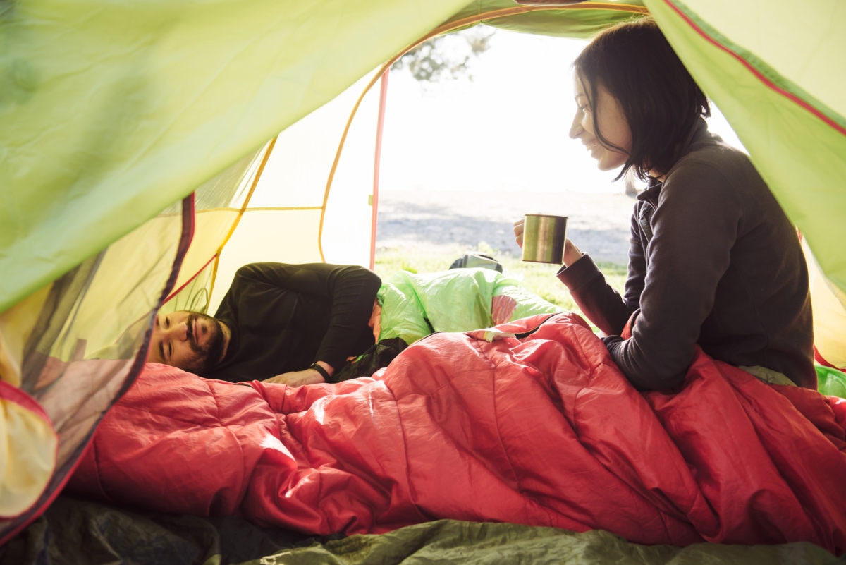 Couple traveling and spending time in tent while drinking coffee in the morning