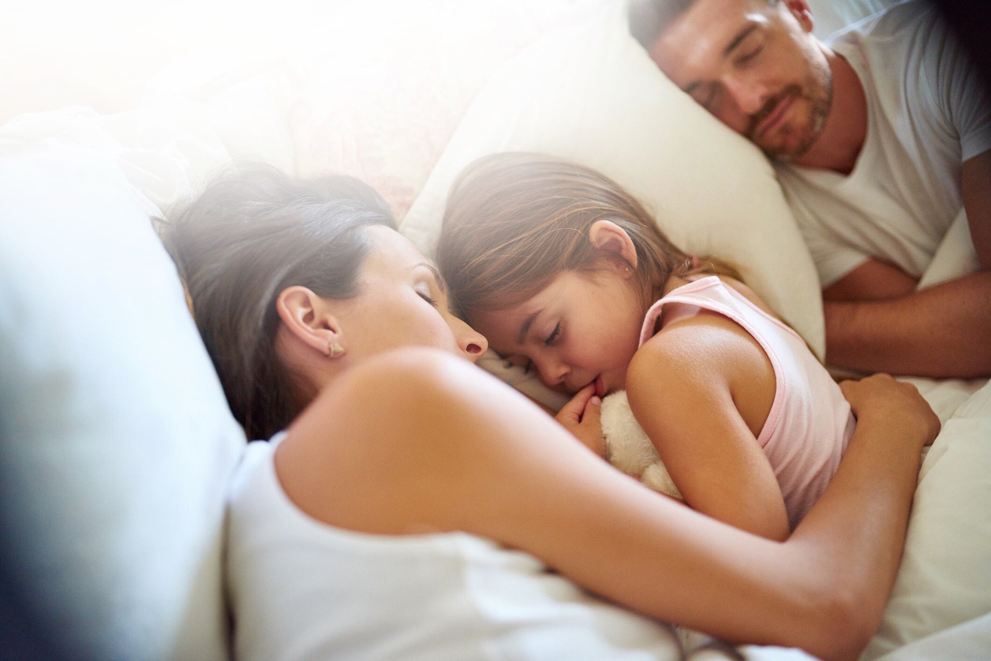 child and parents sleeping on bed