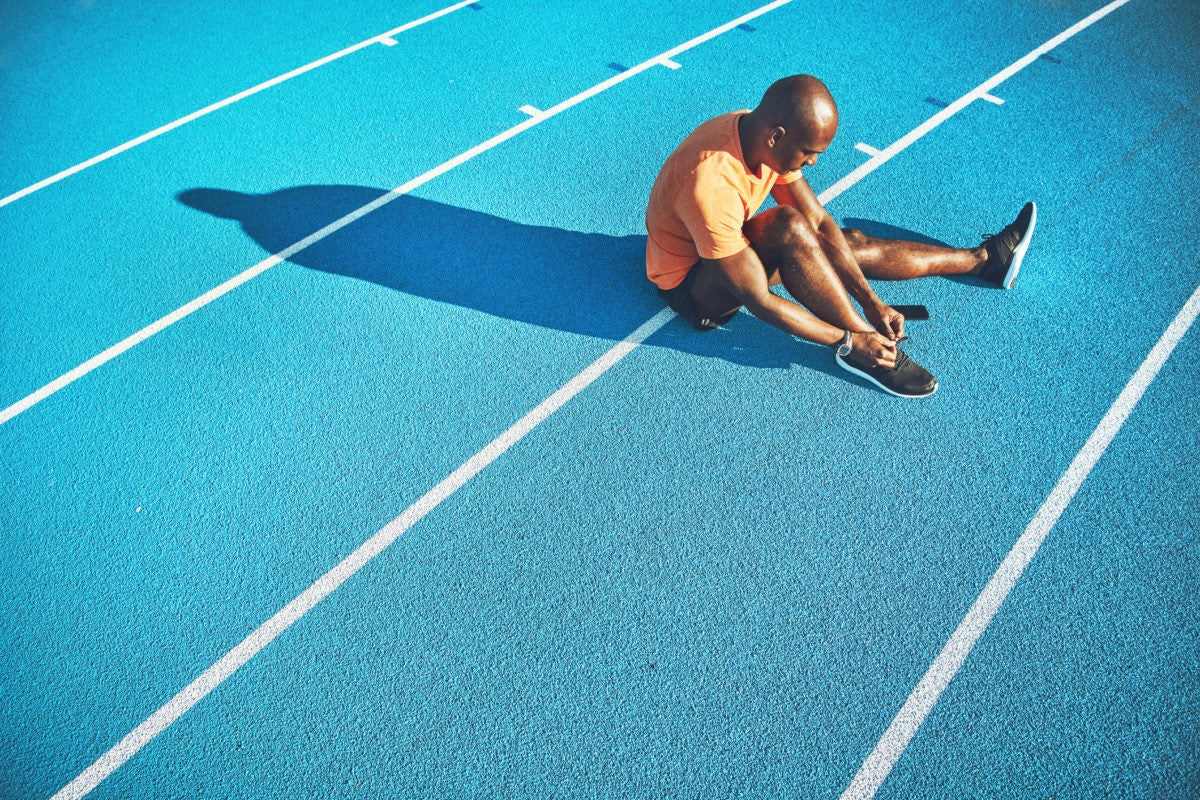 Man tightening his shoe laces sitting on the ground on a running track