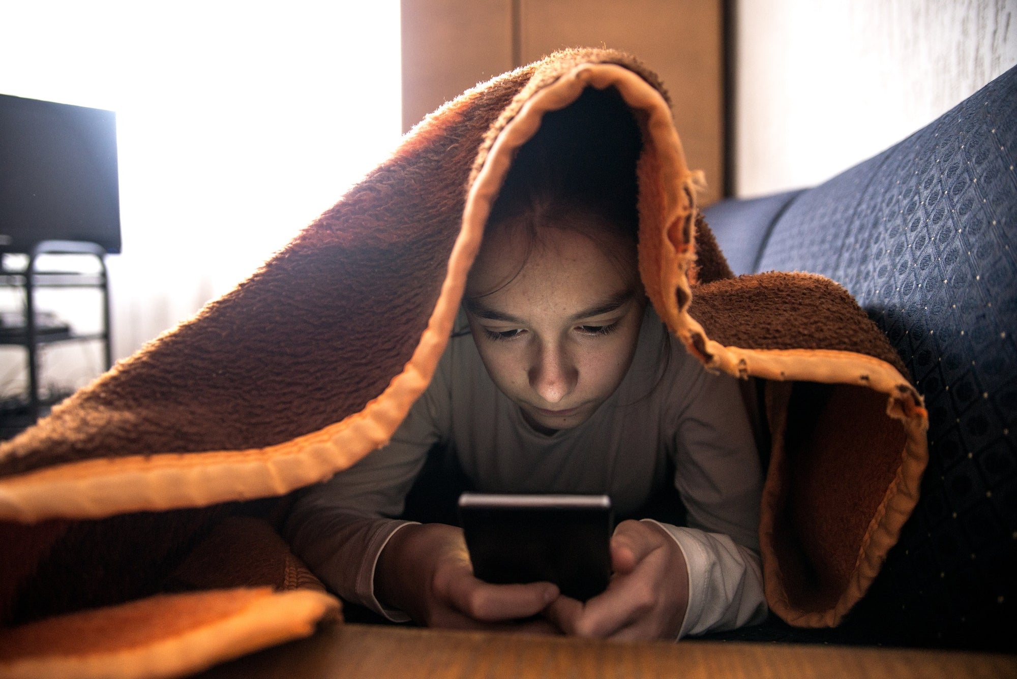 A girl using phone under the blanket