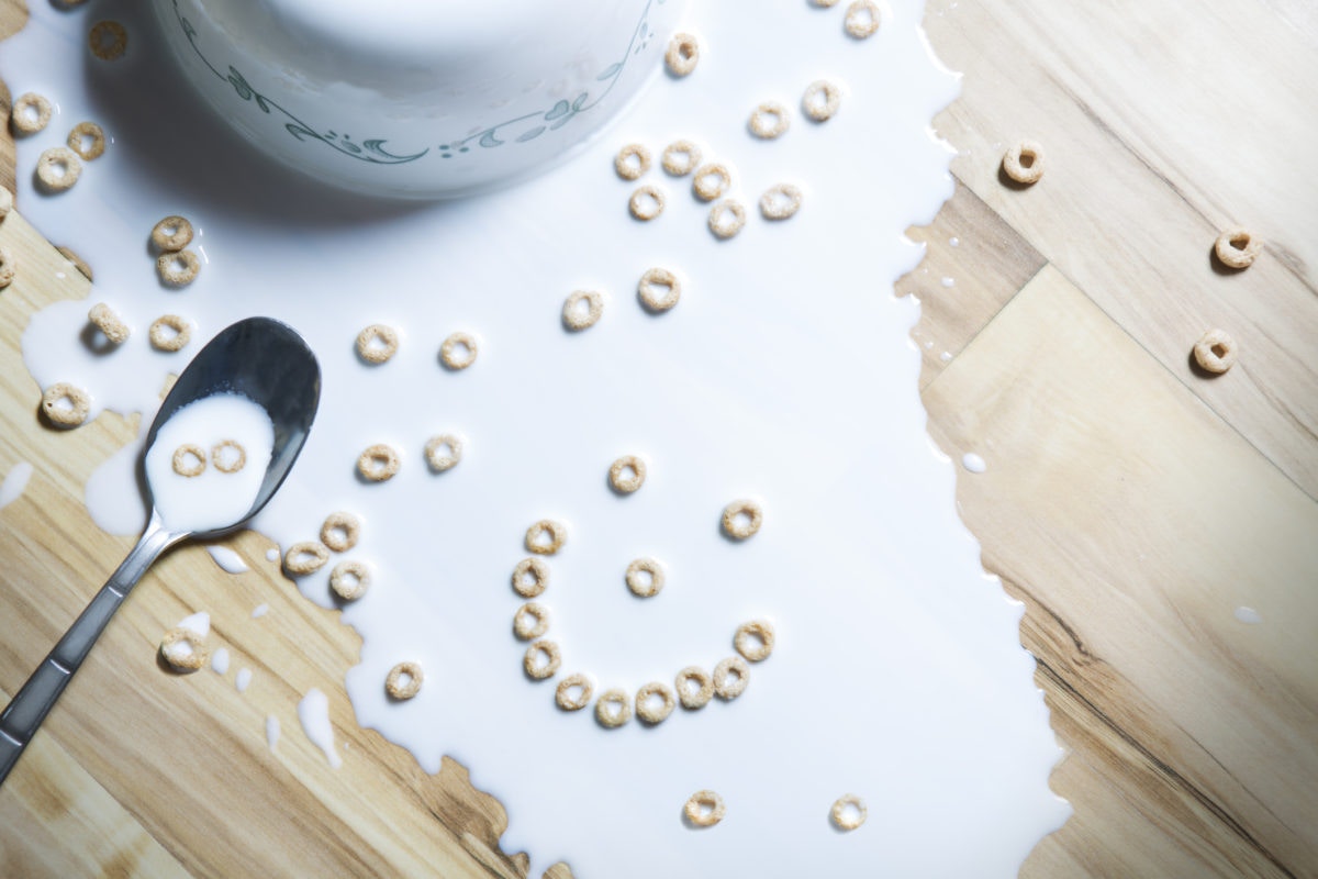 milk spilled over table, cookies in bowl and spoon also spilled