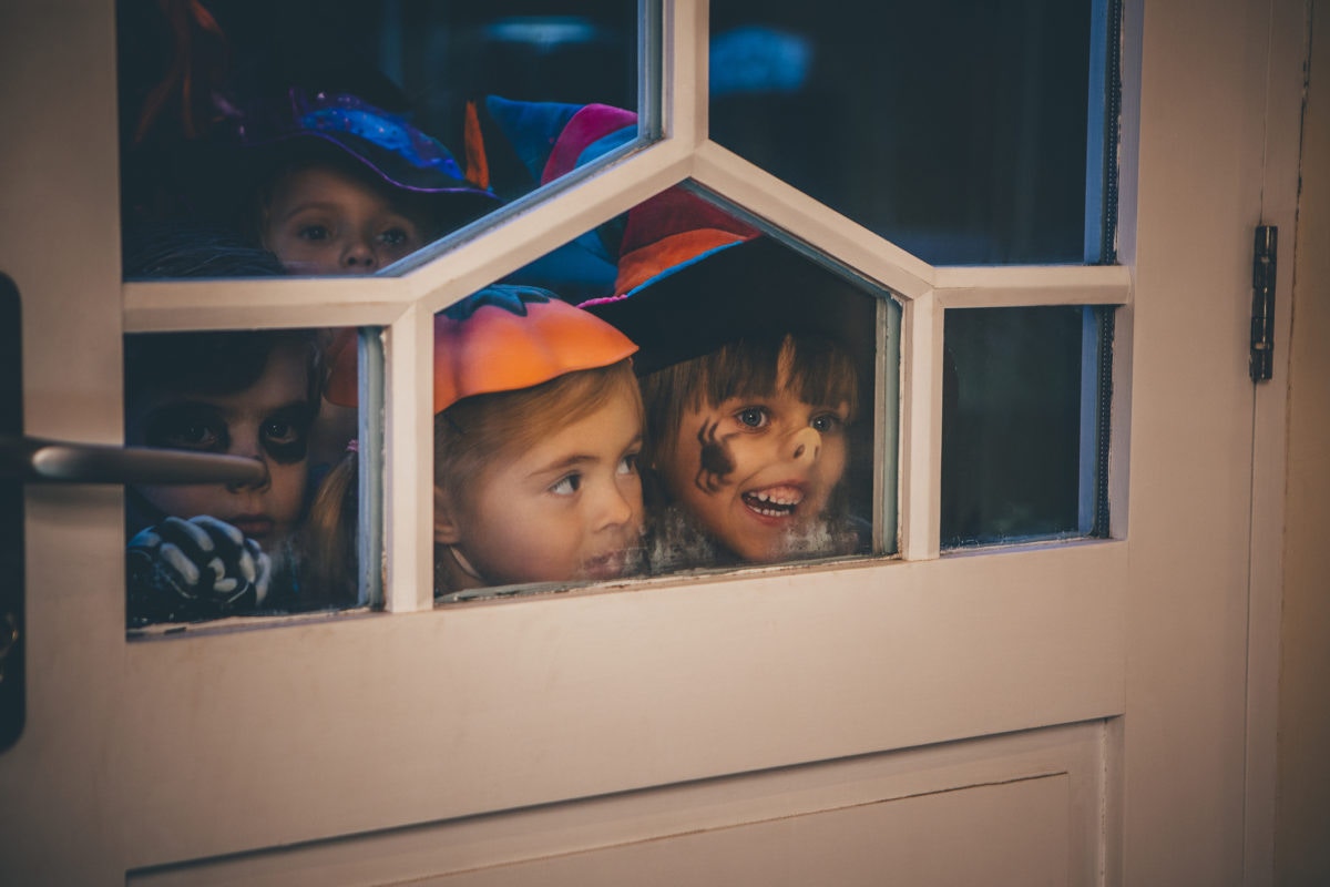 Children sneeking from behind door on halloween