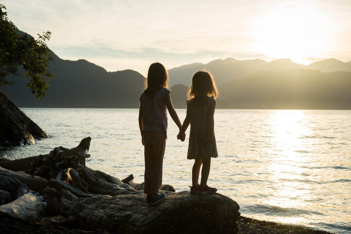 sisters holding hands looking at the lake