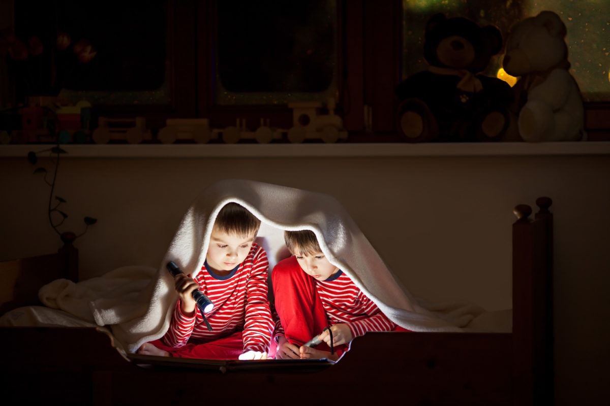 boys reading book under blanket with a torch light