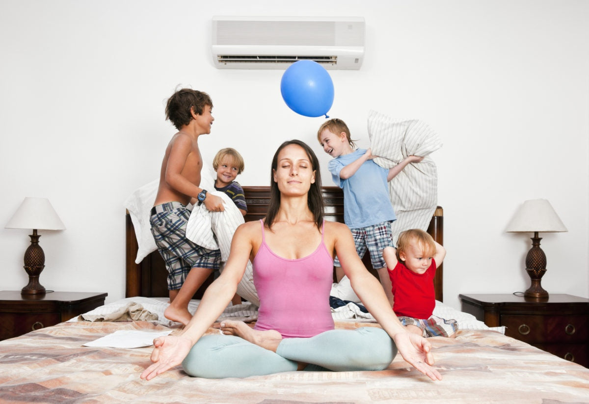 mom trying to be calm in a yoga pose while kids play around her on a bed