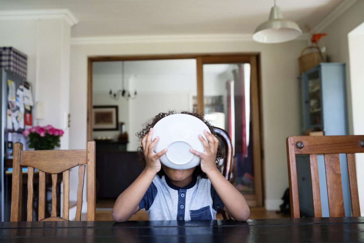 kid at a table holding a bowl of cereal