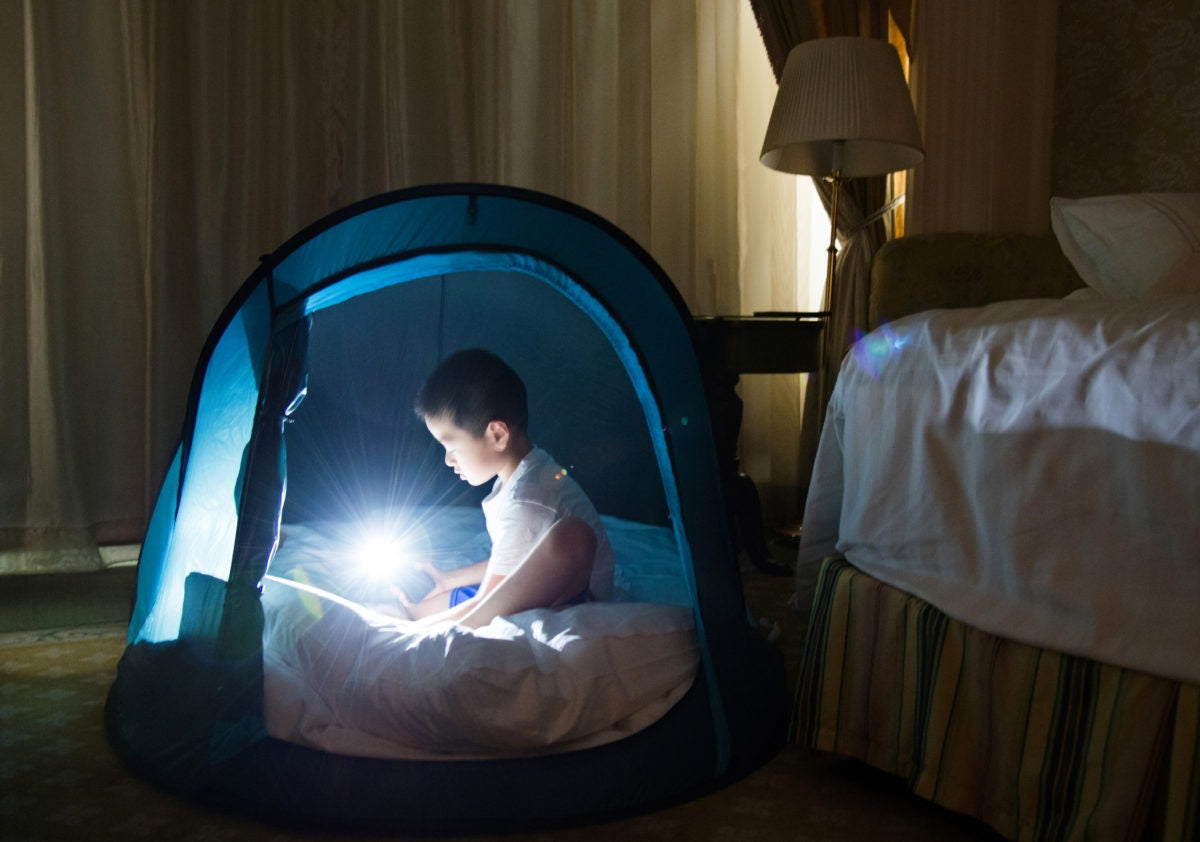 A kid is sitting in a tent house with torche light on