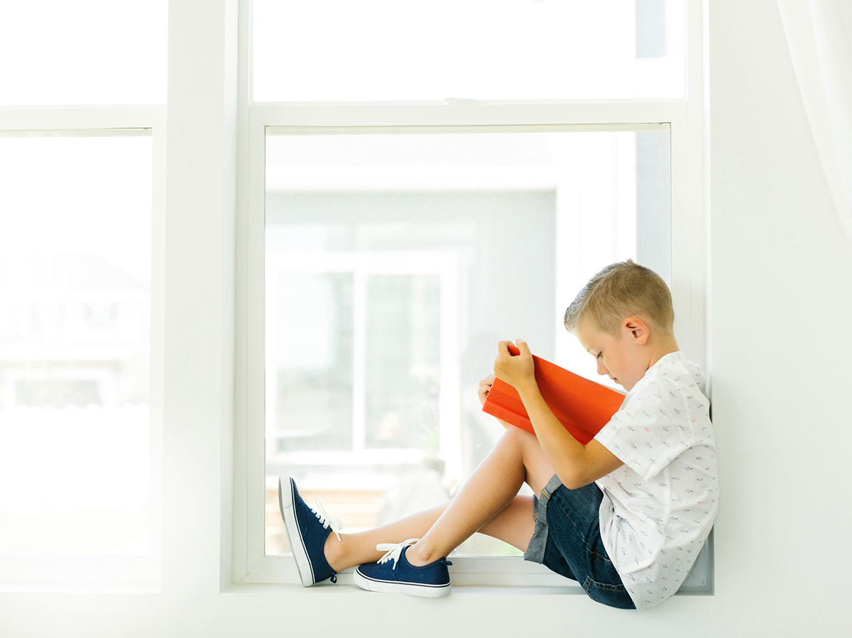 A kid reading a book, sitting at thw window