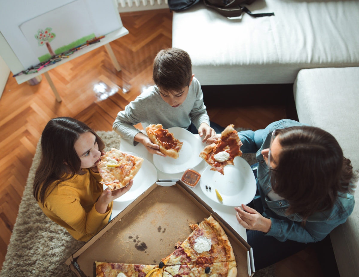 mother, son and daughter eating pizza at home