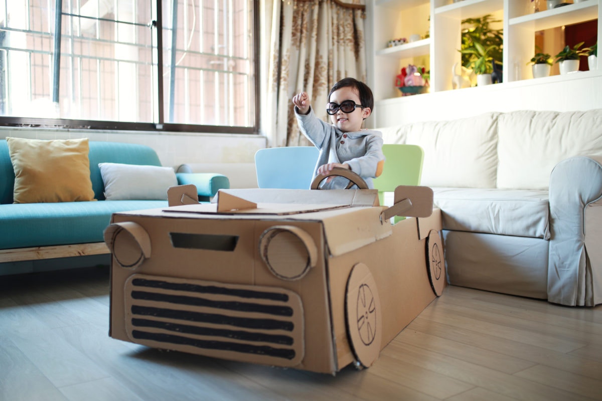 young boy driving his homemade cardboard car in living room