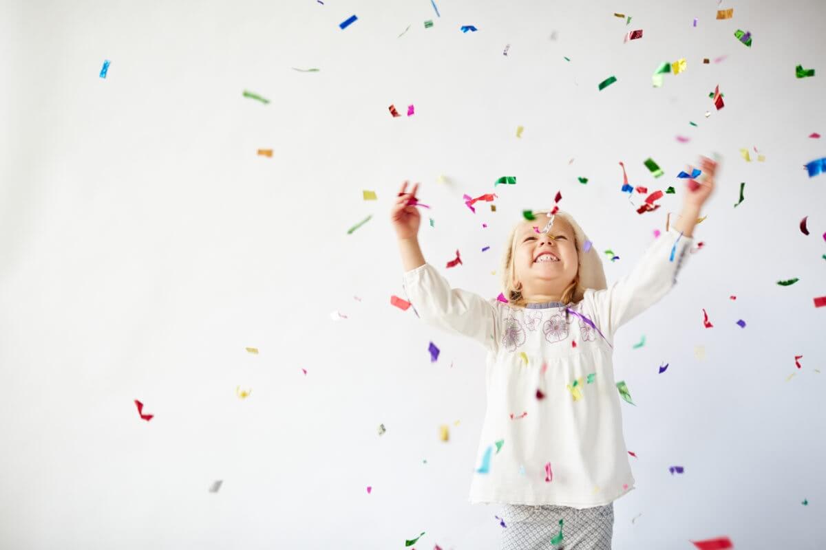 Happy little child girl with colorful confetti on white background