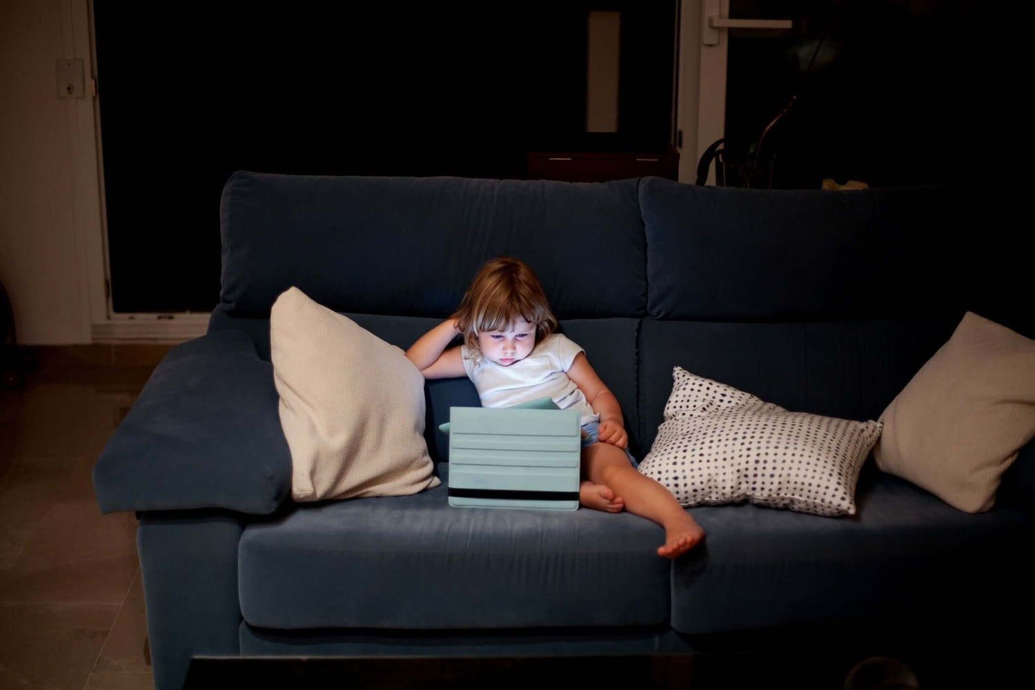 little girl sitting on sofa watching movie on tablet