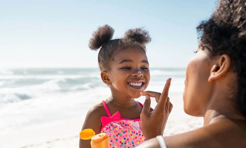 mother applying sunscreen on cute little black girl