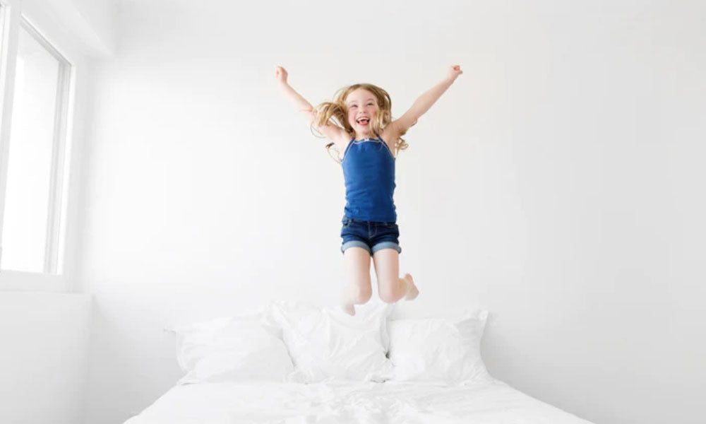 happy little girl wearing blue dress jumping on bed