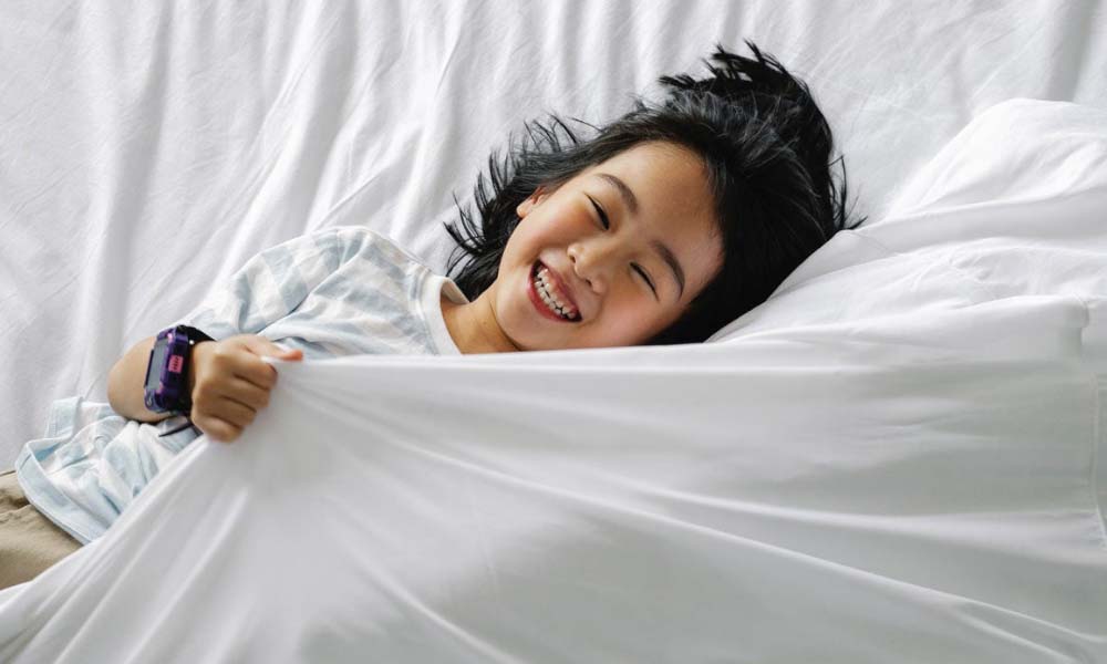 young girl happy in bed with white sheets