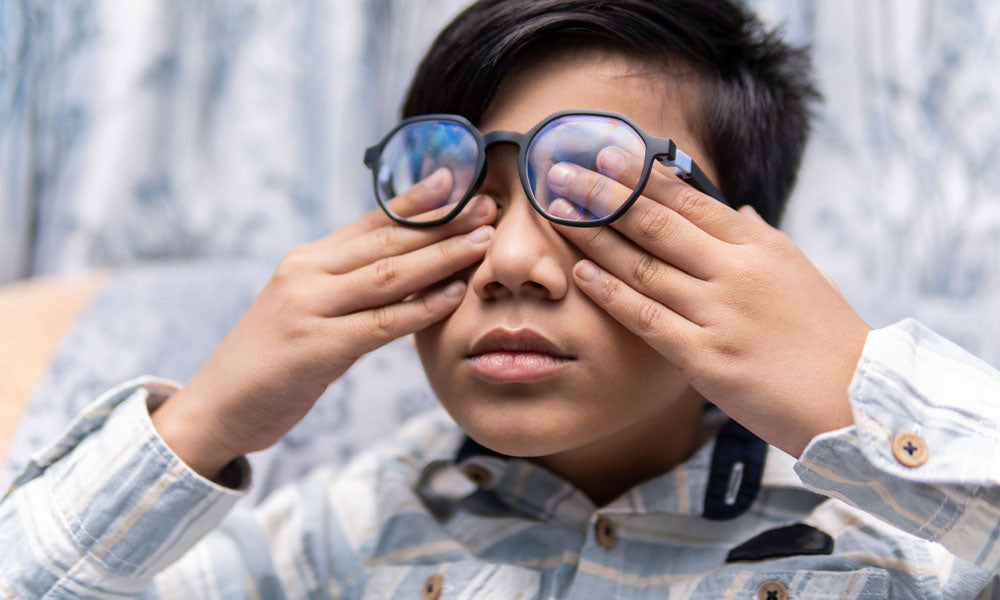 little boy in eyeglasses rubbing his eyes